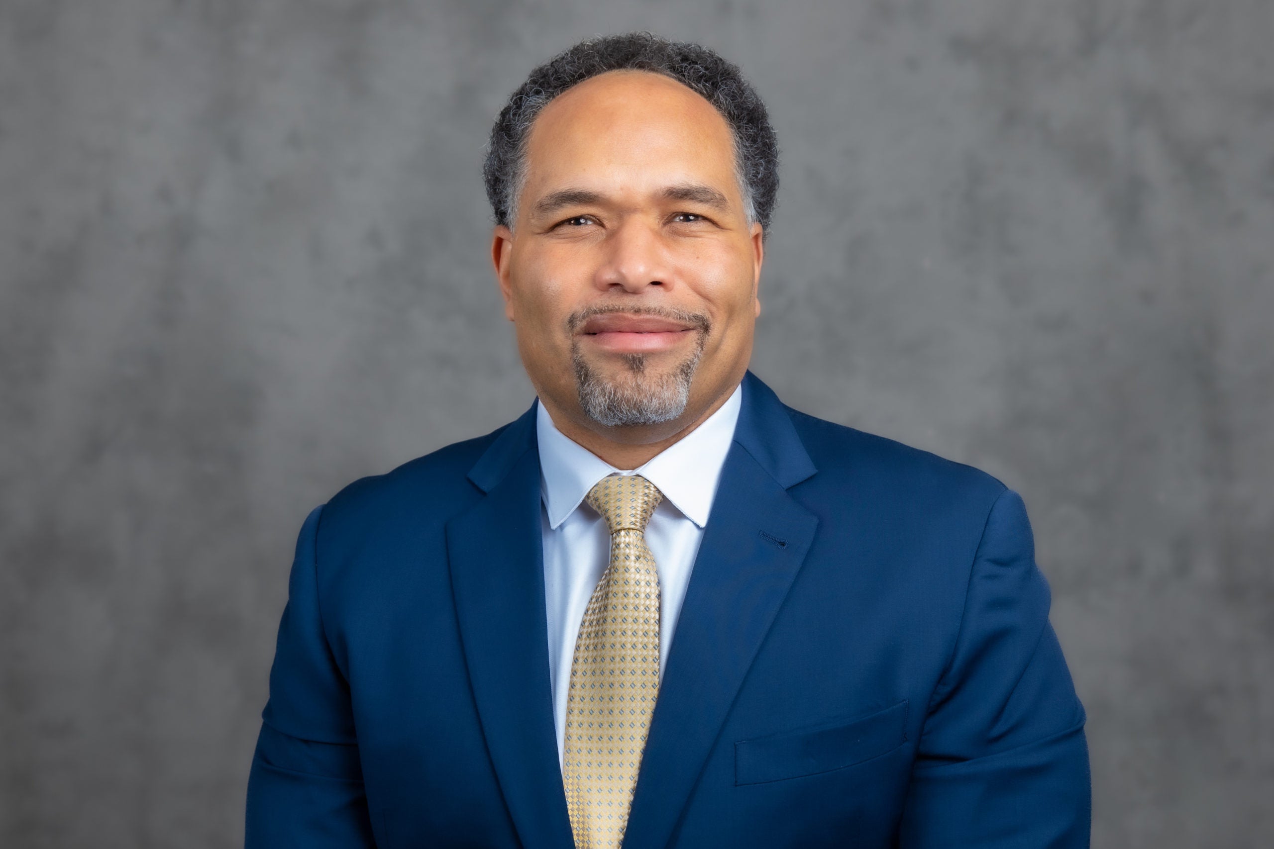 Photo of Jay Darr. He is smiling and wearing a blue suit and a gold tie.